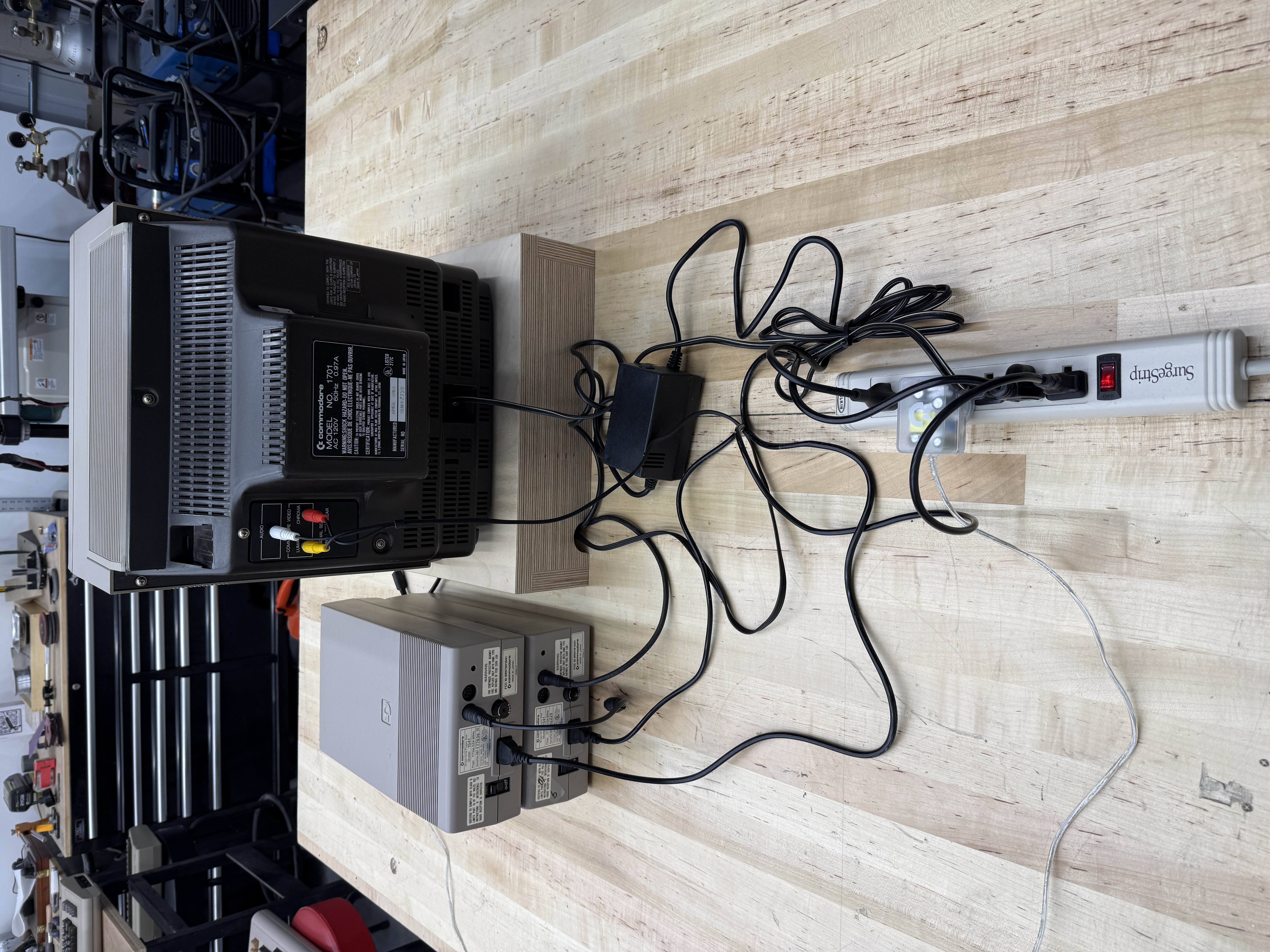A Commodore 64 system from behind: 1701 monitor, two stacked 1541 floppy drives, the C64 power brick, and a tangle of cables running into a power strip