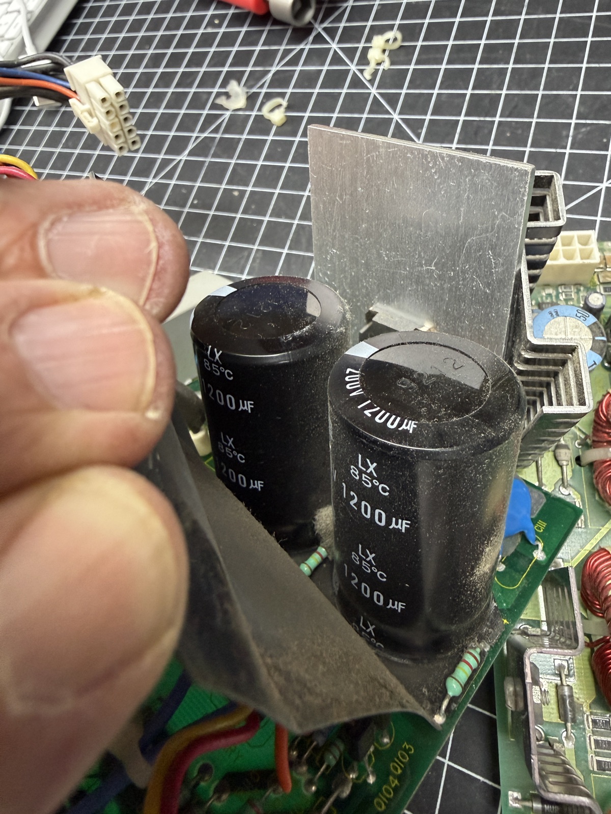 Peeling back the insulating shroud to reveal the original C108 and C109, two 200V 1200µF cans, on the PEC4044B main board