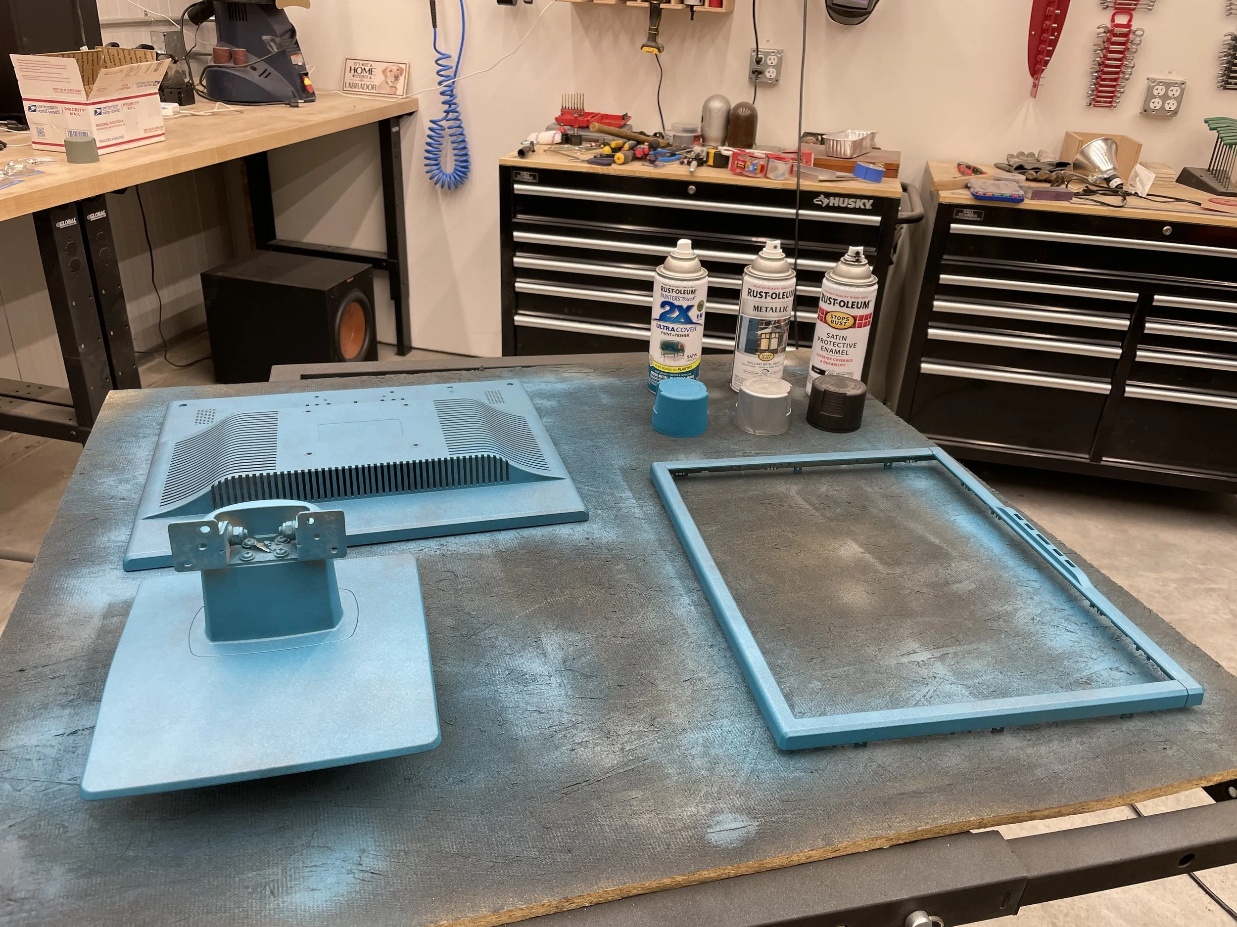 All monitor parts primed in light blue, staged on the paint bench with Rust-oleum cans ready