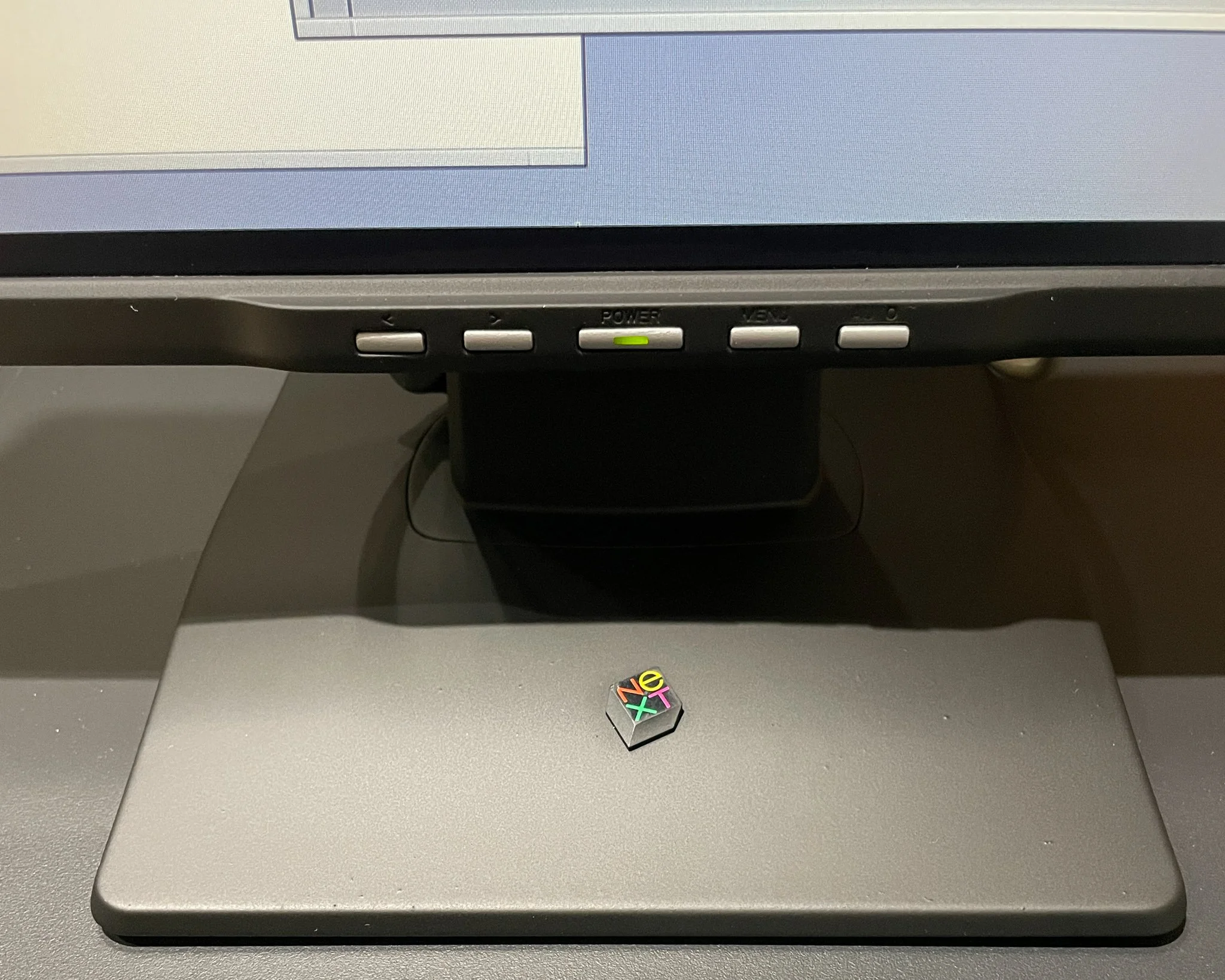 Close-up of the salvaged NeXT logo cube positioned on the painted monitor stand, with the front control buttons visible above