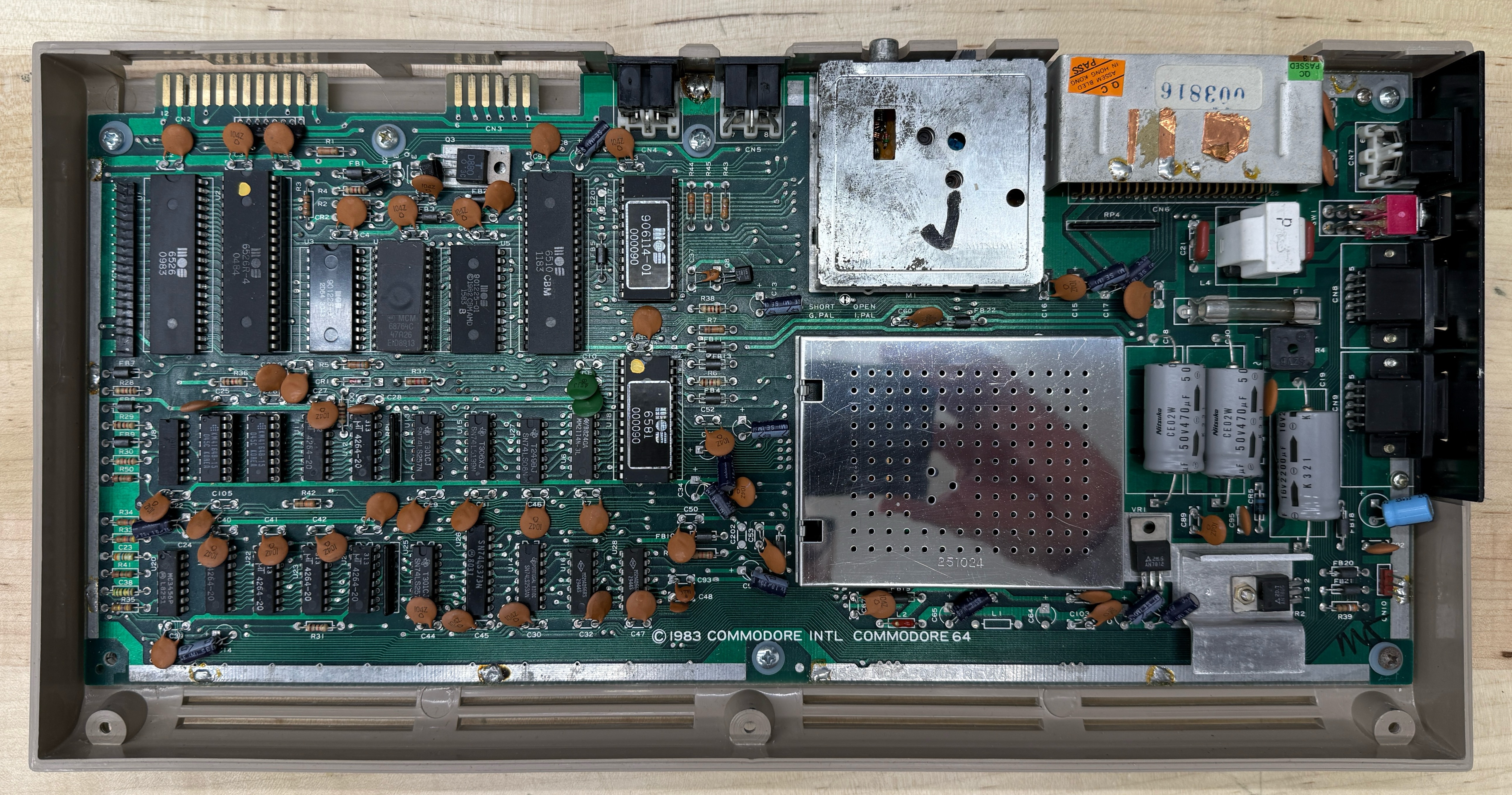 The motherboard of an original Commodore 64 with the top shielding removed, showing the through-hole DIP chips, RF modulator can, and 1983 Commodore 64 silkscreen
